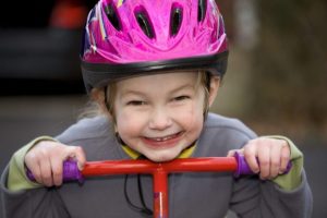 A young girl with a bicycle helmet riding a scooter